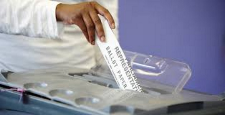 Close up view of a man's hand putting a ballot paper into a ballot box.