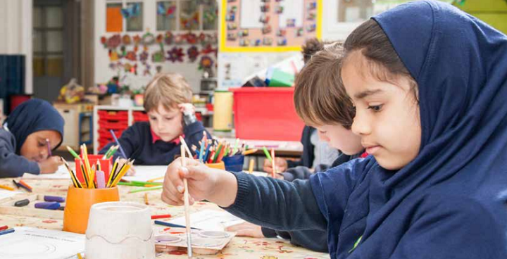 Primary school children sitting around a large desk painting pictures