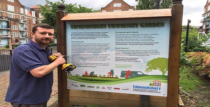 Bearded volunteer uses cordless screwdriver to fit printed side of noticeboard that explains recycling on Edmundsbury Estate