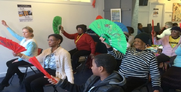 small group of women of different ages practising therapeutic exercise with large green oriental paper fans