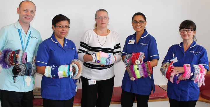 Nurses holding twiddle mitts - simple colourful knitted cuffs, to which a range of items, including ribbons, buttons or beads, can be sewn.
