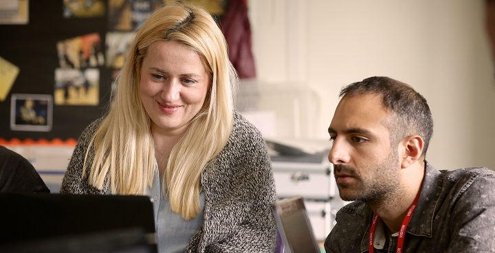 Blonde women and dark bearded short haired man wearing a lanyard look at screen as part of IT training session