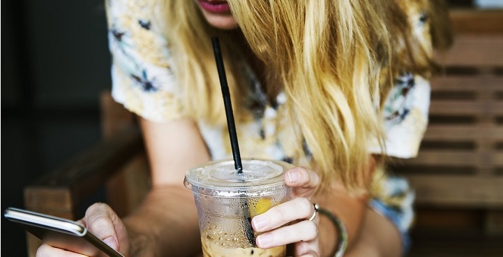 Close up of girl's hair covering face,with mobile in right hand and half-finished drink with plastic straw in left