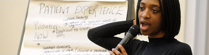 Black Thrive: woman with microphone talks in front of whiteboard with 'The Patient experience' as a header to brainstormed ideas