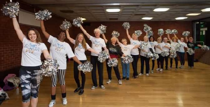 A row of people Silver Cheerleading with their pom poms.