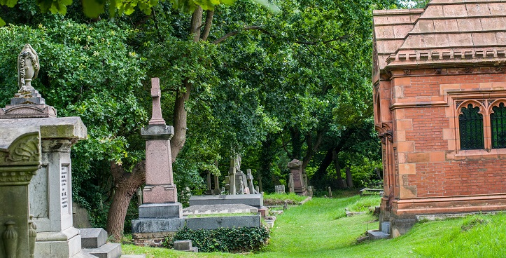 L-R red grantite cross, stone coffin shaped memorial against green lawns and trees - Victorian graves in West Norwoood Cemetery