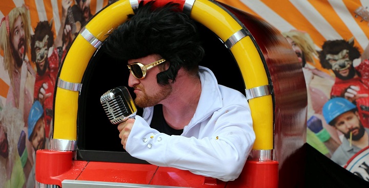 Elvis Presley impersonator lip-synching with vintage microphone in 1950s jukebox styles puppet show booth