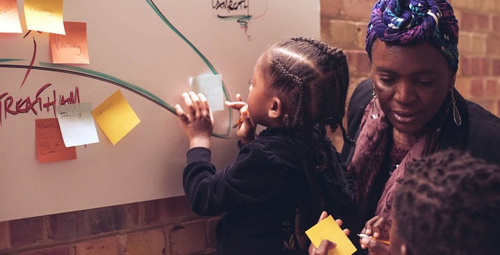 Child and two ladies writing ideas on post-its, at a culture bid workshop.