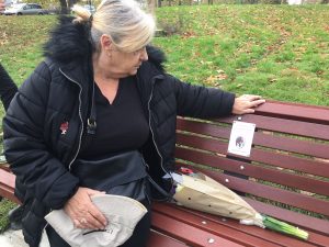 Sitting on the new bench installed in memory of Les Rhodes, his neighbour Christine Carney reads the plaque while holding a hat owned by the terror attack victim