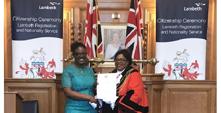 Resident Laurencia Kwanga (green dress, hair up)is handed her UK naturalization certificate by Lambeth Mayor Cllr Marcia Cameron in red robes and chain Jan 12 2018 in the refurbished Lambeth Town Hall Council Chamber