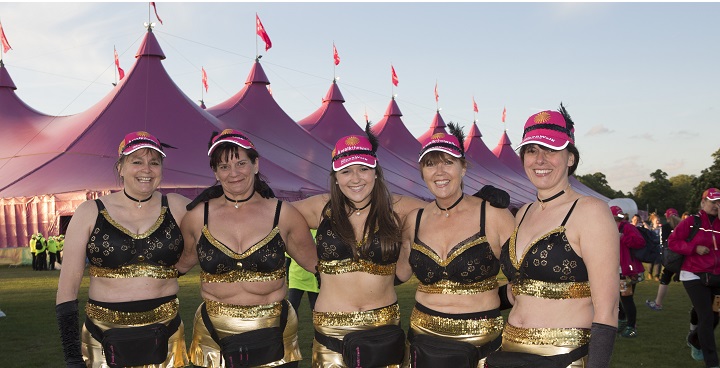 Women with linked arms and black bras decorated with gold stand outside the pink 'Moonwalk' breast cancer charity walk base tent on Clapham Common