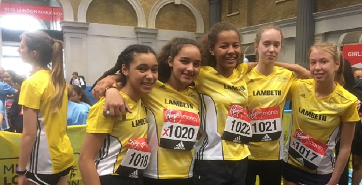 girls in yellow running tops with team numbers stand shoulder to shoulder at the end of the race