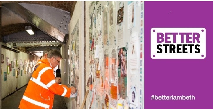 Workman in orange hi-viz and white hard hat with posters on the white walls of Herne Hill underpass