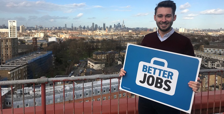 Cllr Matthew Bennett holding the Better Jobs sign on the roof at International House