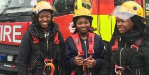 3 x fire cadets in safety helmets giving the camera 'thumbs up' in front of a red fire engine