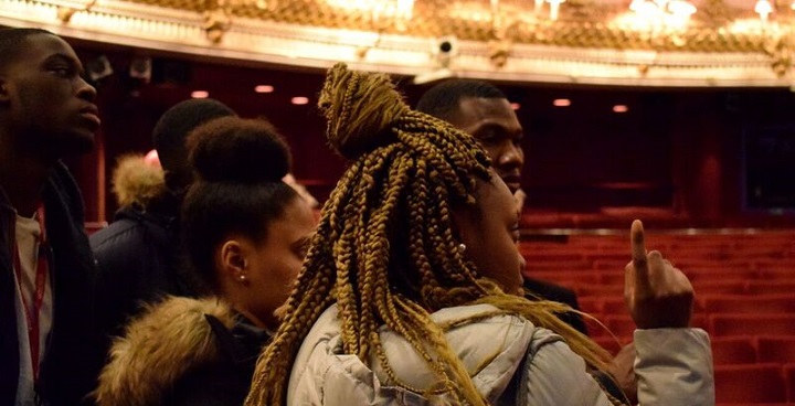 Group of teenage boys and girls looking around the red chairs and bright lights of the stalls on a visit to the Rotal Opera House, Covent Garden