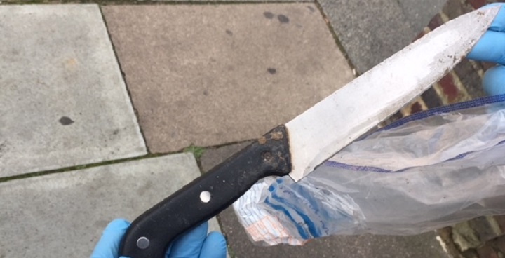 Police officer's hands in blue plastic gloved holding large kitchen knif beleived to be a used as a weapon - collected from a 'weapons sweep' by council enforcement officers and Met. Police in Lambeth