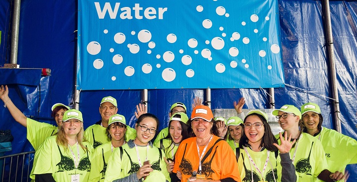 women volunteers in yellow hi-vis tops with water for the walkers on breast cancer charity 'walk the walk's annual 'moonwalk' under a blue sign with bubbles and the word 'water' in white