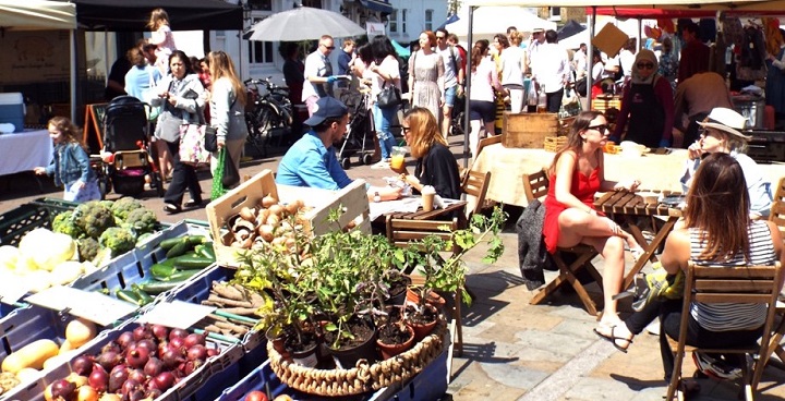 People at cafe tables and browsing plant stalls at Herne Hill Sunday market on a sunny day
