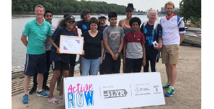 Angell Town-based Brixton Wings rowing club receive an award from Olympic Champion Andrew Triggs Hodge and MP Susan Elan Jones, all standing in a line by the water's edge July 2018