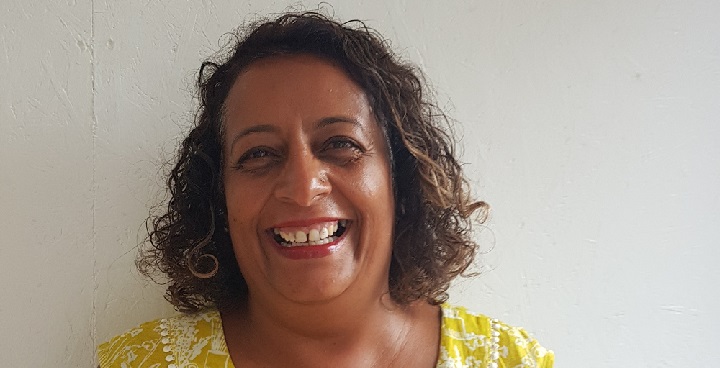 Laughter Yoga convenor/teacher Zeenat grins at the camera with loose hair and yellow dress