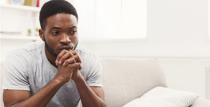 A young man sitting on the edge of a sofa, looking concerned.