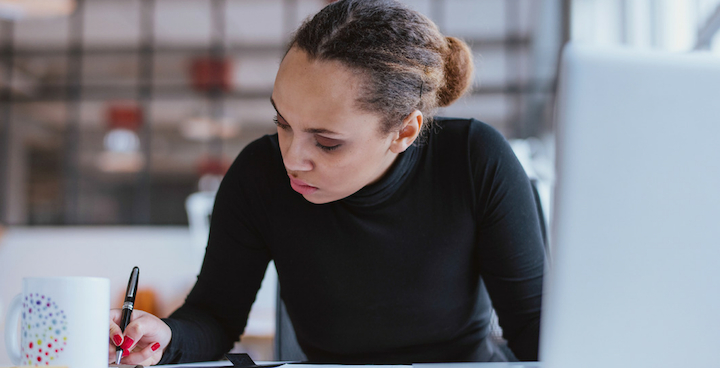 A young woman sitting at a desk with a note pad and laptop.