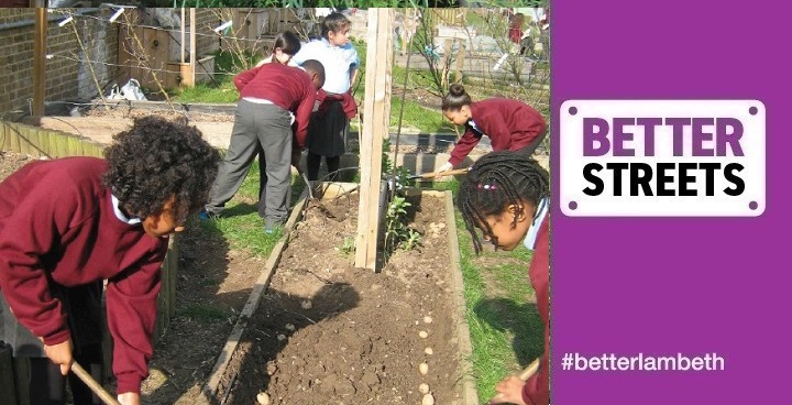 Primary school children in maroon uniform jumpers and grey trousers digging the gardens at Hitherfield Primary School