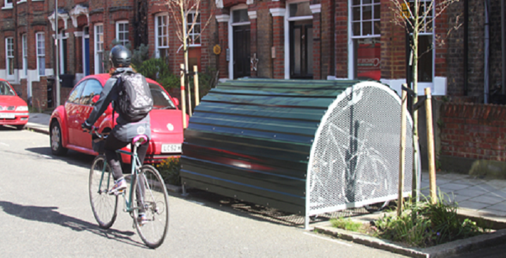 Lady cycles past bike hangar on Lambeth street