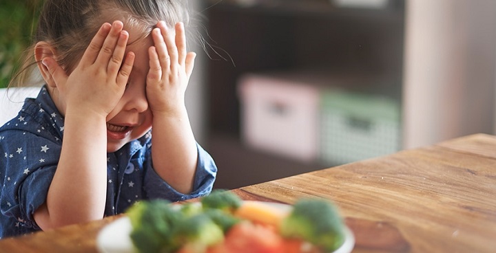 Young girl sitting at dining table putting hands over eyes to aboid seeing a plate of carrots and cauliflower - part of a Lambeth-wide campaign to advertise veg to 7-12 year olds