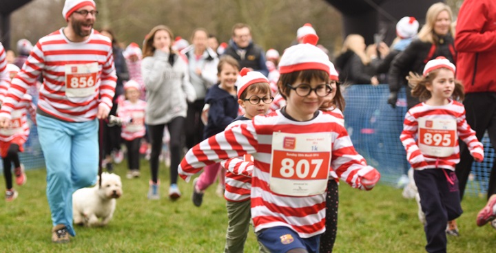 children & adults dressed as kids book character where's wally in red & white striped jumpers, round black spectacles and bobble hats join fundraising fun run on Clapham Common