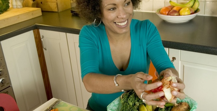 Woman in kitchen scraping veg peelings into biodegradable liner in bin caddy