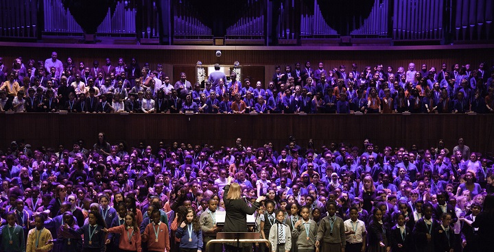 Choir of kids on stage in front of organ pipes in South Bank's Festival Hall with conductor (back to us) - floodlit in purple -