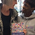 Cllr Meldrum (in leopard print coat) with parent carer Denise holding 'Girls and Autism' book at Autism Action Day