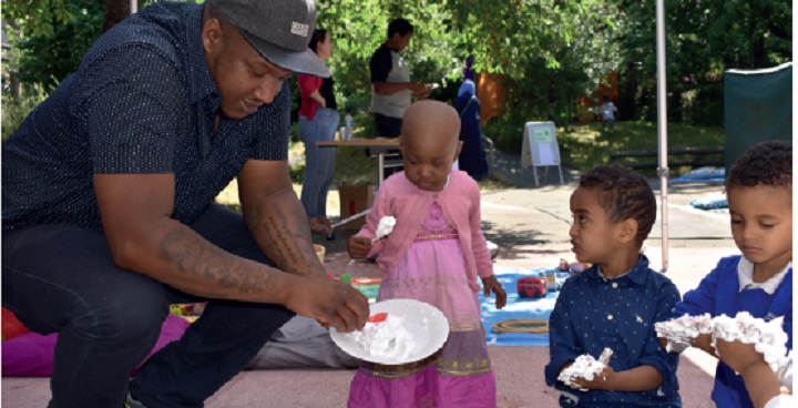 afro-Caribbean adult with 3 x toddlers playing with shaving foam on paper plates. child in centre wearing pink, two others blue