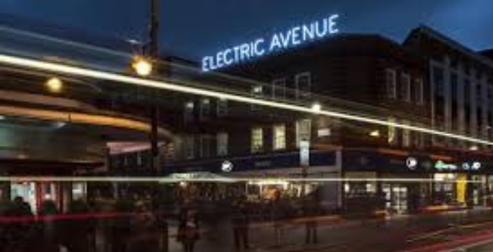 Brixton high street at night with electric avenue street named street light on top of building.