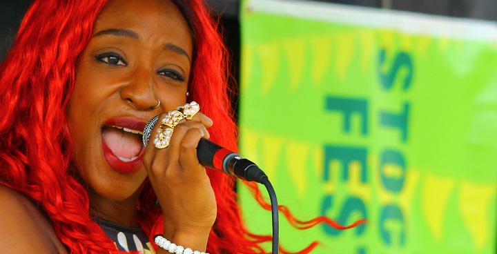 Singer at Stockwell festival holding microphone in had with bracelet; her hair is dyed red, she has a pierced nose