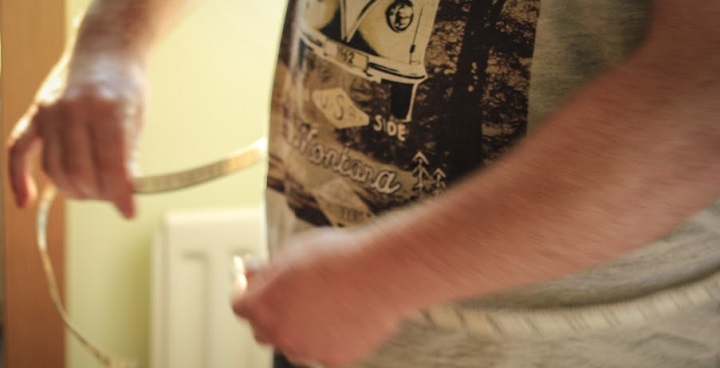 man in volkswagen t-shirt putting tape measure round waist to measure it