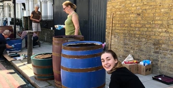 Women painting whiskey barrels blue to use as planters in Stockwell's Tradescant Road
