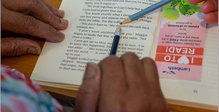 Adult literacy - learning to read a book with help to point out words one at a time with a pencil and bookmark