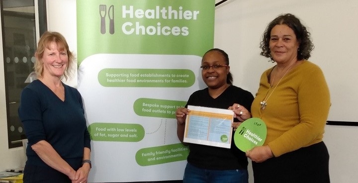 he first Healthier Choices award holder, Terrie Ann Scott of Home N Away café,  receiving her certificate and window sticker from LEAP Director Laura McFarlane and Liza Ctori, Senior Community and Environmental Health Officer, Lambeth.