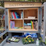 Lou's Little Library with books on shelves, plants to share 