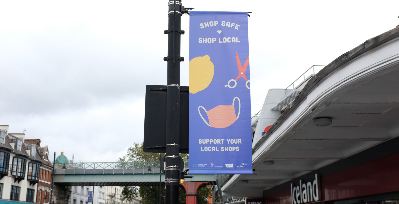 A 'shop safe shop local' lamp post banner on Brixton Road