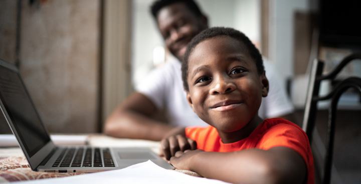 Young boy sat with father at a desk smiling