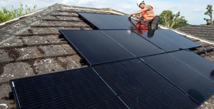 Solar panels being fitted on roof by worker in orange hig vis