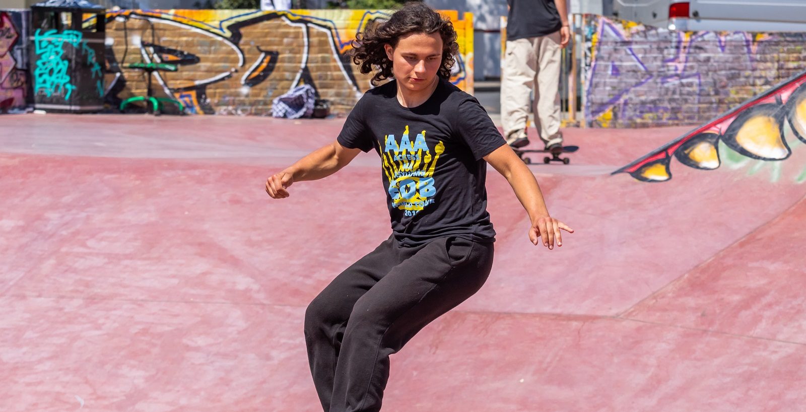 skateboarder with long hair, black t-shirt, jeans