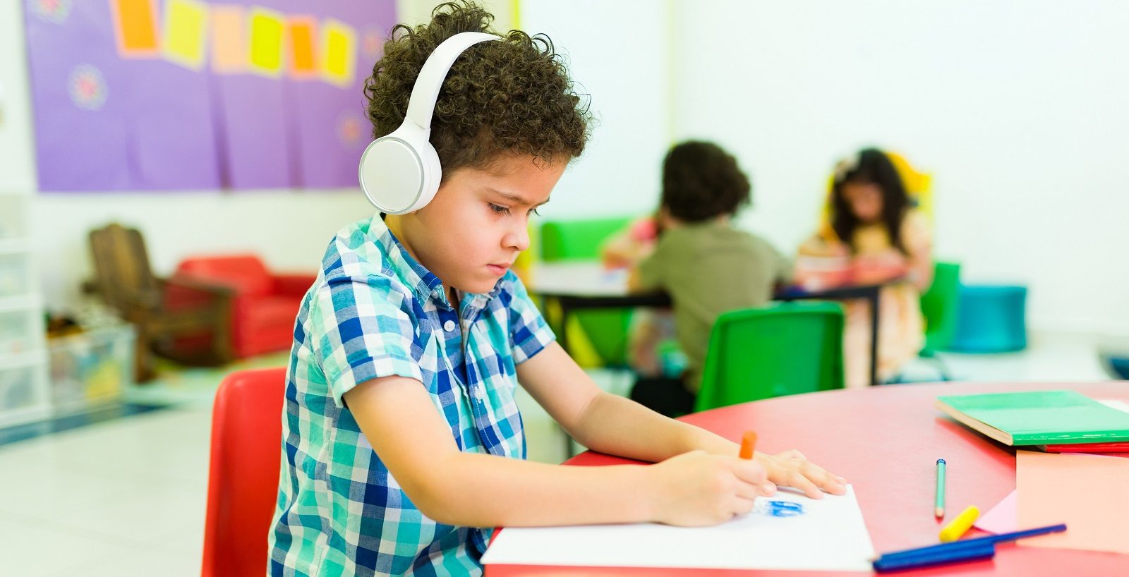 stock photo of boy in green and blue check shirt wearing headphones and writing in an A4 pad