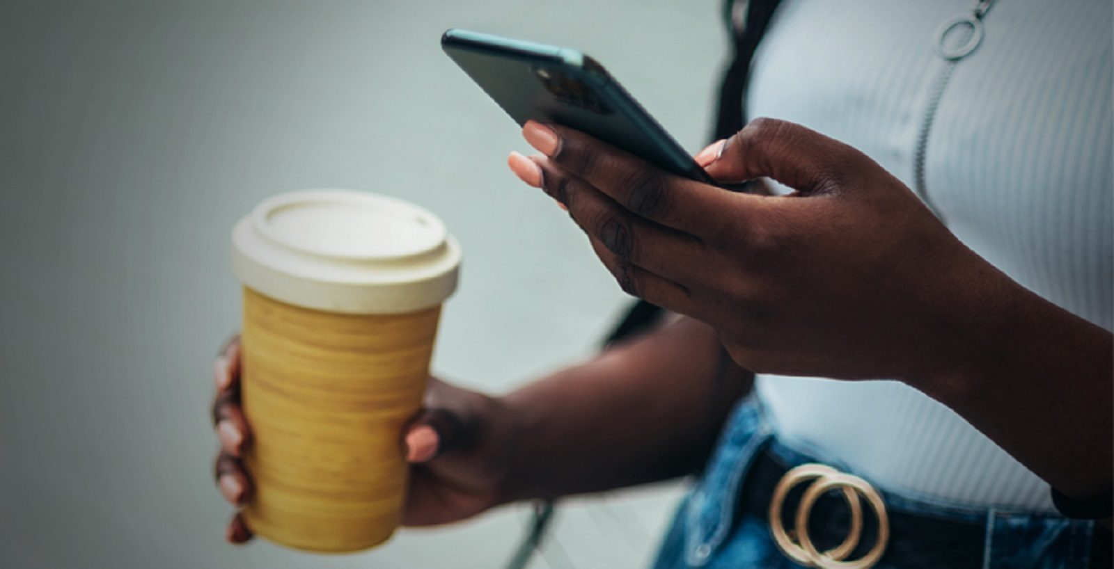close up of woman's hands holding a mobile phone in left hand and takeaway coffee in right