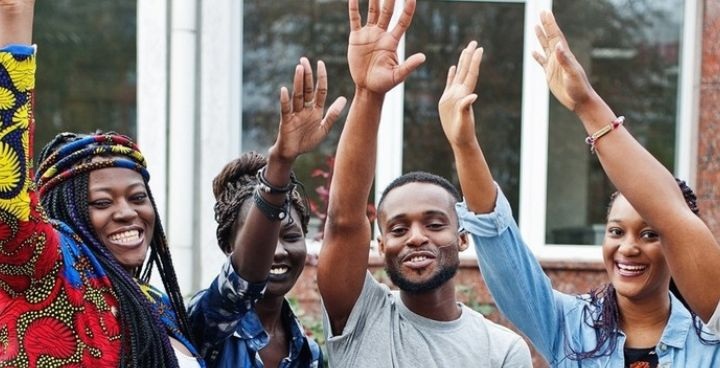 Stock photo of 4 x young Black people standing outside raising hands
