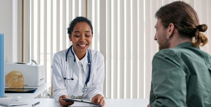 Female health expert smiles as she talks to male patient in treatment room
